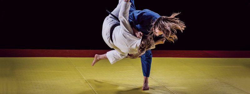 Two women having a judo fight, one is throwing the other one.