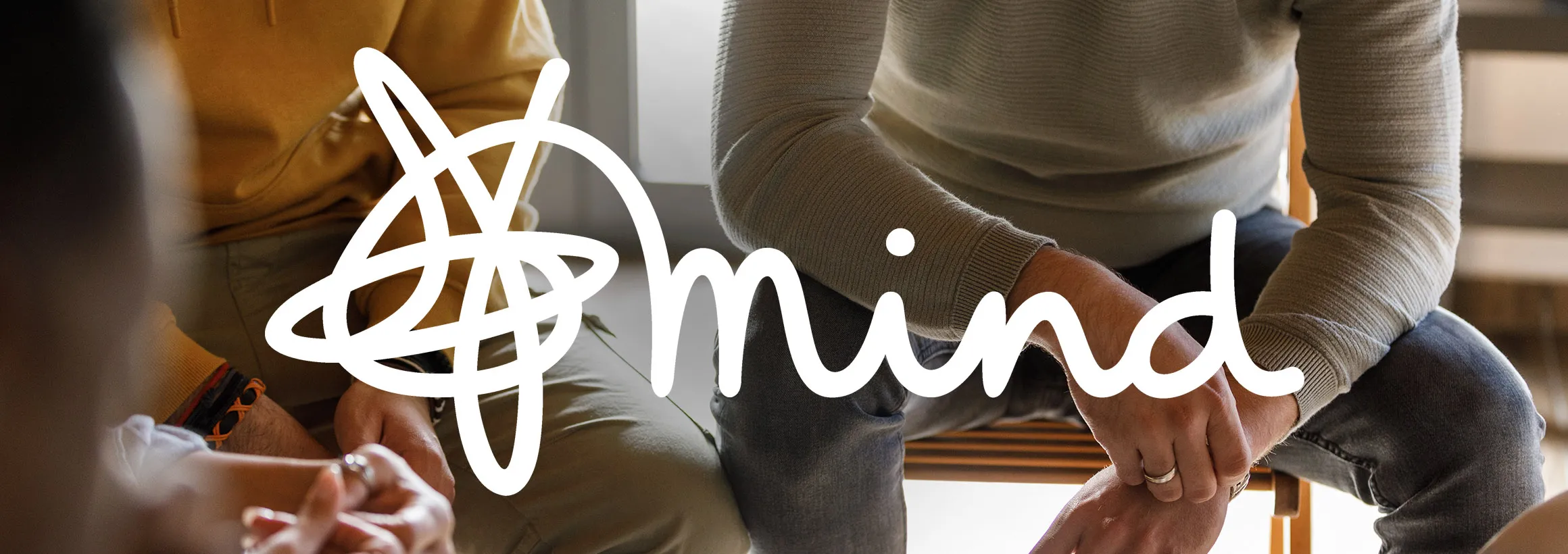 Mind logo over a close up of people talking - they are seated and you can just see their arms, hands and laps