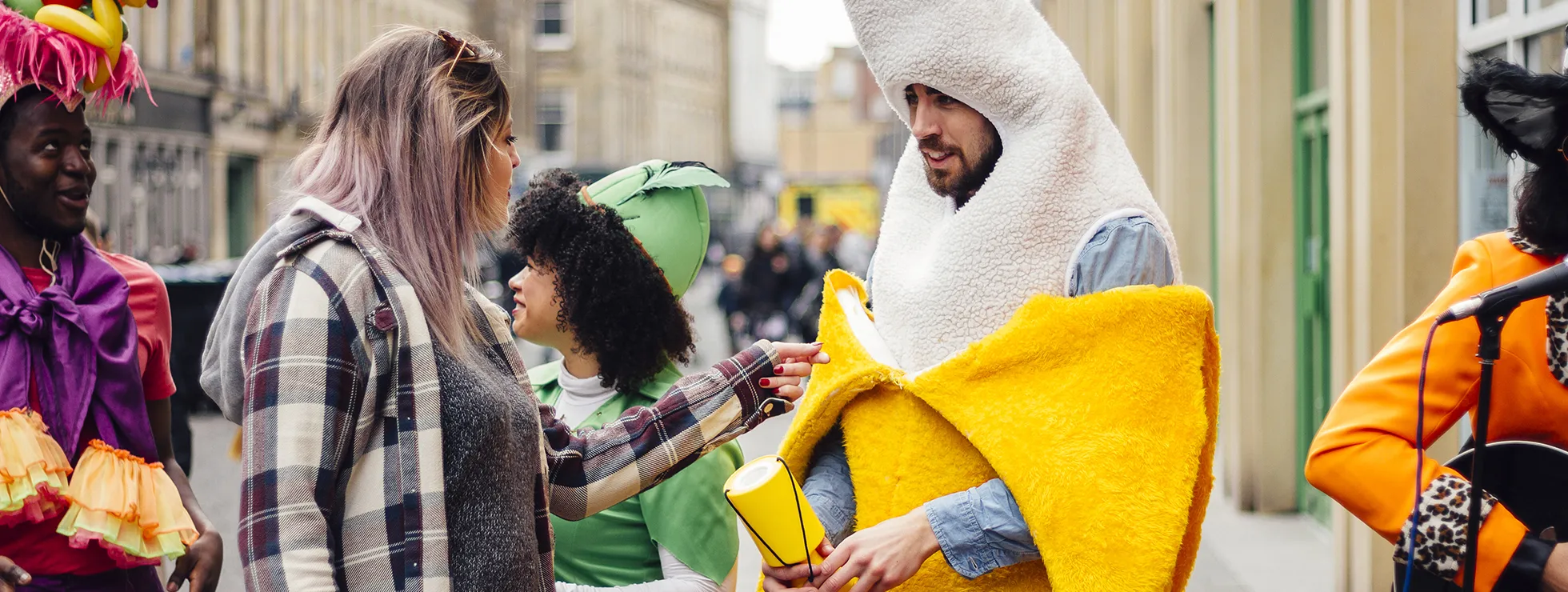 A guy dressed as a banana with a charity collecting tin, talking to other people in costumes at a local carnival event